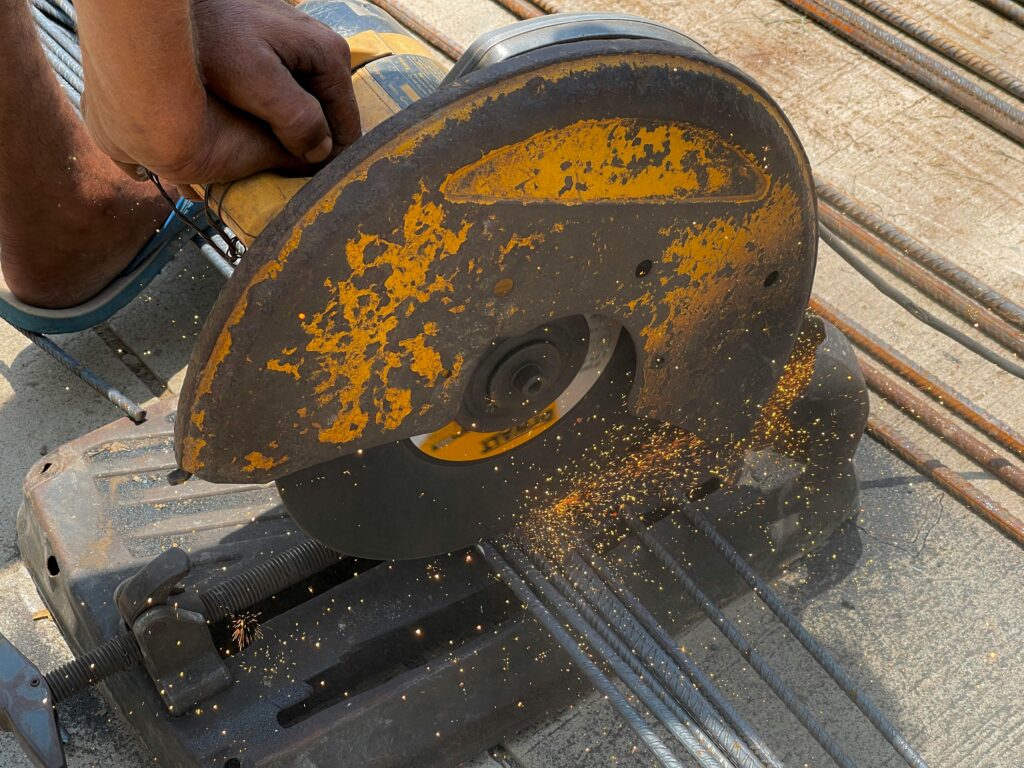 A detailed view of an angle grinder cutting metal rods outdoors in Rasulpur, India.